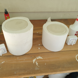 Two cylindrical plaster moulds on a wooden table are filled to the brim with liquid clay