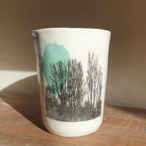 A large white porcelain cup with a black silhouette image of trees partly covering a light green coloured shape