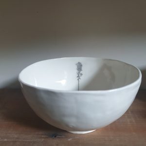 A white porcelain bowl sits on a wooden shelf. An image of a tree is printed on the inside of the bowl.